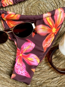 Tropical floral bikini bottom in deep purple on a woven mat with summer accessories