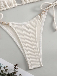 Detail einer weißen gerippten Bikinihose mit goldener Strasskette und Bindebändern