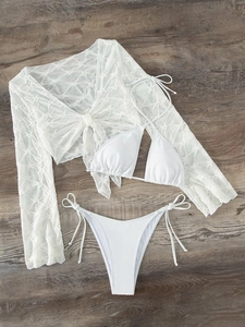 Flat lay of a white three-piece bikini set with sheer lace cover-up on wood background
