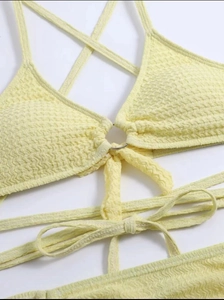 Détail du haut de bikini jaune à texture gaufre avec anneau métallique et nœud décoratif