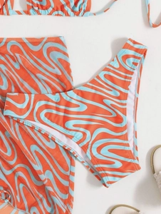 Detail view of a 3-piece bikini set with orange wave print and matching beach skirt
