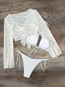 Flat lay of white three-piece bikini set with textured long sleeve cover-up on wood