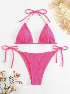 Flachbild von pinkem Ripp-Bikini mit Metallkette und Strasssteinen auf weißem Hintergrund