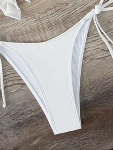 Close-up of white bikini bottoms with side tie strings on a vintage wooden background