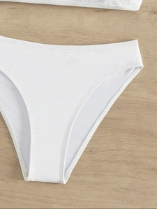 Detailed flat lay of white high-waisted bikini bottoms on a brown wood texture