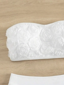 Detailed close-up of white 3D floral rosettes on a strapless bikini top with fine stitching