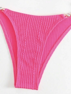 Detail der gerippten pinken Bikinihose mit verstellbaren Trägern und Goldperlen-Verzierung