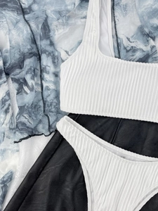 Flat lay of a white ribbed bikini set with a grey marble mesh cover-up on black leather