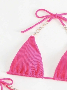 Detail eines rose-pinken Bikinis mit Texturstoff und Goldkette mit Kristall-Strasssteinen