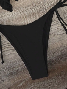 Detailed flat lay of black bikini bottoms with adjustable side-tie and textured fabric