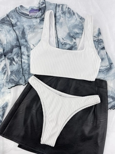 Flat lay of white ribbed bikini set with black faux leather mini skirt on marble fabric