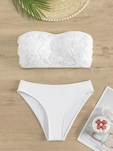 Detail of white bandeau bikini top with 3D rose petal appliques on wooden background