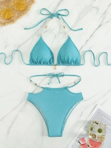 Vue à plat d'un bikini pailleté bleu avec breloques perles et coquillages sur marbre