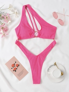 Bikini rose asymétrique avec anneaux dorés et texture côtelée posé sur fond blanc
