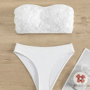 White two-piece bikini featuring 3D floral bandeau top and minimalist bottoms on wood surface