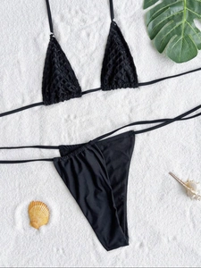 Flat lay of black mesh bikini set with halter top and high-cut bottom on sand background