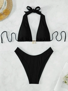 Flat lay of black ribbed bikini with golden shell charms on marble background