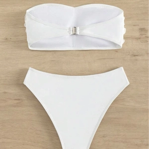 White bandeau bikini set with silver back buckle and high-waisted bottoms on wood