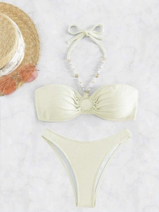 Set bikini verde chiaro con catena di perle e accessori estivi su marmo bianco