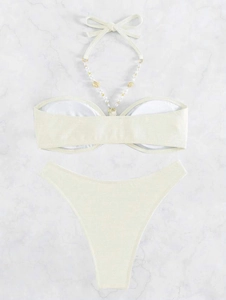 Dettaglio di un bikini crema con conchiglie dorate e perle sui laccetti del collo
