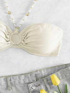 Dettaglio top bikini con spalline di perle e conchiglie su fondo in marmo
