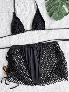 Detailed view of black three-piece bikini set with a long mesh cover-up skirt on white fur