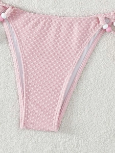 Détail d'un bas de bikini rose avec tissu texturé et liens latéraux ornés de perles
