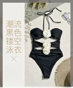 Flat lay of black halter one-piece swimsuit featuring 3D white rose flowers and cut-outs