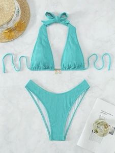 Flat lay of ribbed turquoise bikini with shell charms on white marble background