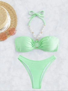 Dettaglio del bikini verde menta con lacci di perline e trama a costine su marmo bianco