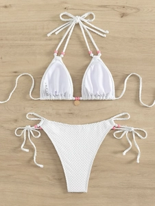 Détail d'un bikini blanc nid d'abeille avec bretelles perlées roses et breloque cœur doré