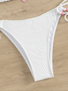 Gros plan sur un bas de bikini blanc texturé avec cordons à perles roses sur le côté