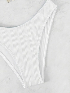 Detail of high-waisted white ribbed bikini bottom with high-cut leg on marble