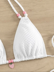 Détail du haut de bikini blanc texturé avec breloque fraise et perles sur les bretelles