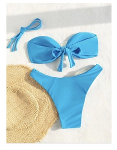 Flat lay of bright blue bikini with bow detail and straw hat on white background