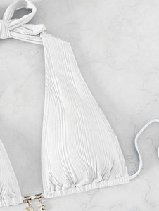 Detail view of white pleated bikini top with gold shell and starfish charms on marble