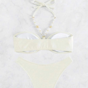 Elegante bikini allacciato al collo bianco crema con catene di perle e conchiglie su marmo