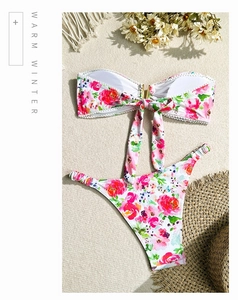 Vue à plat d'un bikini bandeau fleuri avec nœud et culotte échancrée sur du sable fin