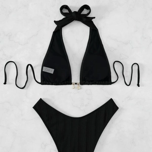 Black halter bikini set with ribbed texture and gold seashell charms on marble surface