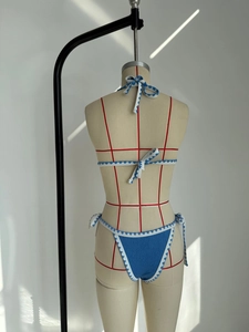 Detail of blue textured bikini set with white zigzag trim and adjustable ties on mannequin