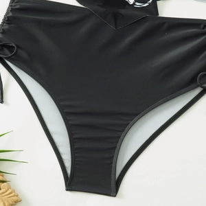 Dettaglio dello slip bikini nero a vita alta con coulisse laterale e stampe