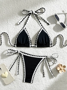 Close-up of black bikini set with white scalloped trim and tie-side details on soft rug