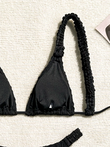 Detail of black bikini top featuring ruched shoulder straps and smooth satin finish