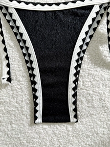 Detail of seersucker bikini bottom with black zigzag lace trim and white piping edges