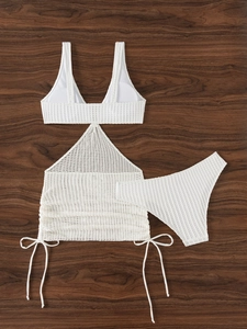 Flat lay of white knit three-piece bikini set with drawstring skirt on wood background