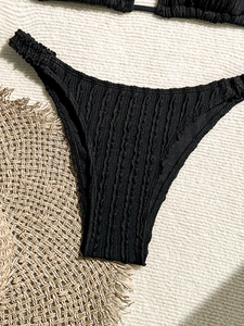 Close-up of black ruched bikini bottoms with textured fabric on a woven beach mat