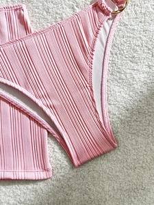 Detail of pink ribbed bikini bottom with gold ring hardware on white faux fur background