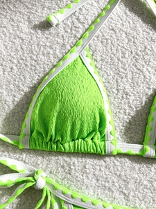 Detail of neon green smocked bikini top with white wavy patterned straps on plush rug