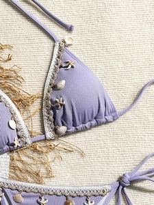 Detail of lavender ribbed bikini with shell and starfish charms on a beige textured background