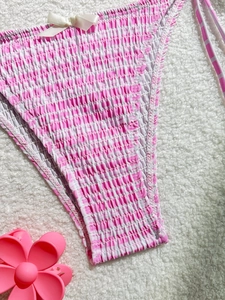 Bas de bikini froncé rose et blanc avec un nœud sur un fond blanc texturé